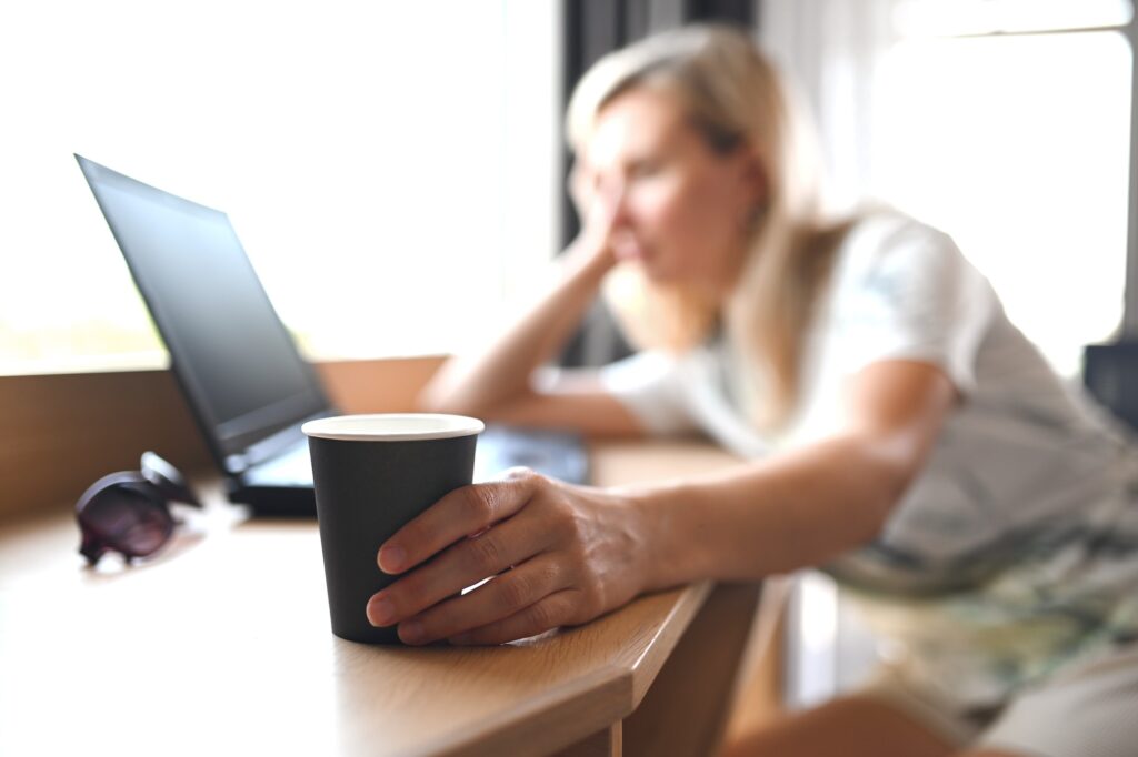 Sad unhappy woman holding a paper cup of coffee at the remote desk and feels stress and burn out